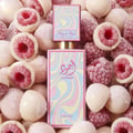 Lattafa Ajwad Pink 2 Pink Creamy Elixir — Botol corak pusaran merah jambu dan pastel dikelilingi buah raspberi bersalut coklat putih dan raspberi penuh.