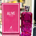 Maison Alhambra Alive Now — A bright pink box with white text and a deer logo sits next to a faceted pink glass perfume bottle with a silver cap. | Maison Alhambra Alive Now — Kotak merah jambu terang dengan teks putih dan logo rusa duduk di sebelah botol minyak wangi kaca merah jambu berfaset dengan penutup perak.