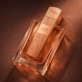 Lattafa Angham Second Song by Lattafa 100ml — Tampilan dekat botol minyak wangi berpenutup berlubang warna emas ros dengan tulisan Arab dan nota muzik, diletakkan di atas permukaan coklat bertekstur.