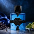 French Avenue Aromatix Magnetiq 100ml — Blue glass perfume bottle with black geometric cap and label, set against a dark blue satin background with lavender, mint, lime, and peppercorns.