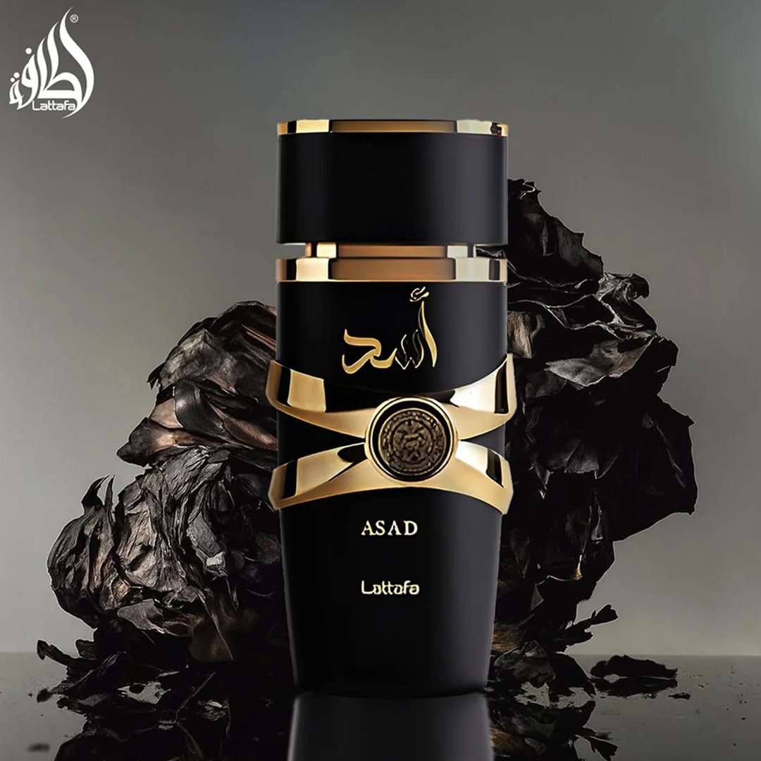 Lattafa Asad Lattafa EDP 100ml Men — Botol minyak wangi hitam dengan perincian emas dan tulisan Arab, berlatar belakang gelap bertekstur seperti kayu terbakar atau arang.
