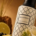 Maison Asrar Belgravia by Maison Asrar Eau de Parfum — Botol putih bercorak geometri hitam, dengan label "BELGRAVIA" dan "ROYAL COLLECTION". Sebiji limau, beri hitam, dan bunga freesia putih kelihatan di latar depan, dengan latar belakang coklat kabur.