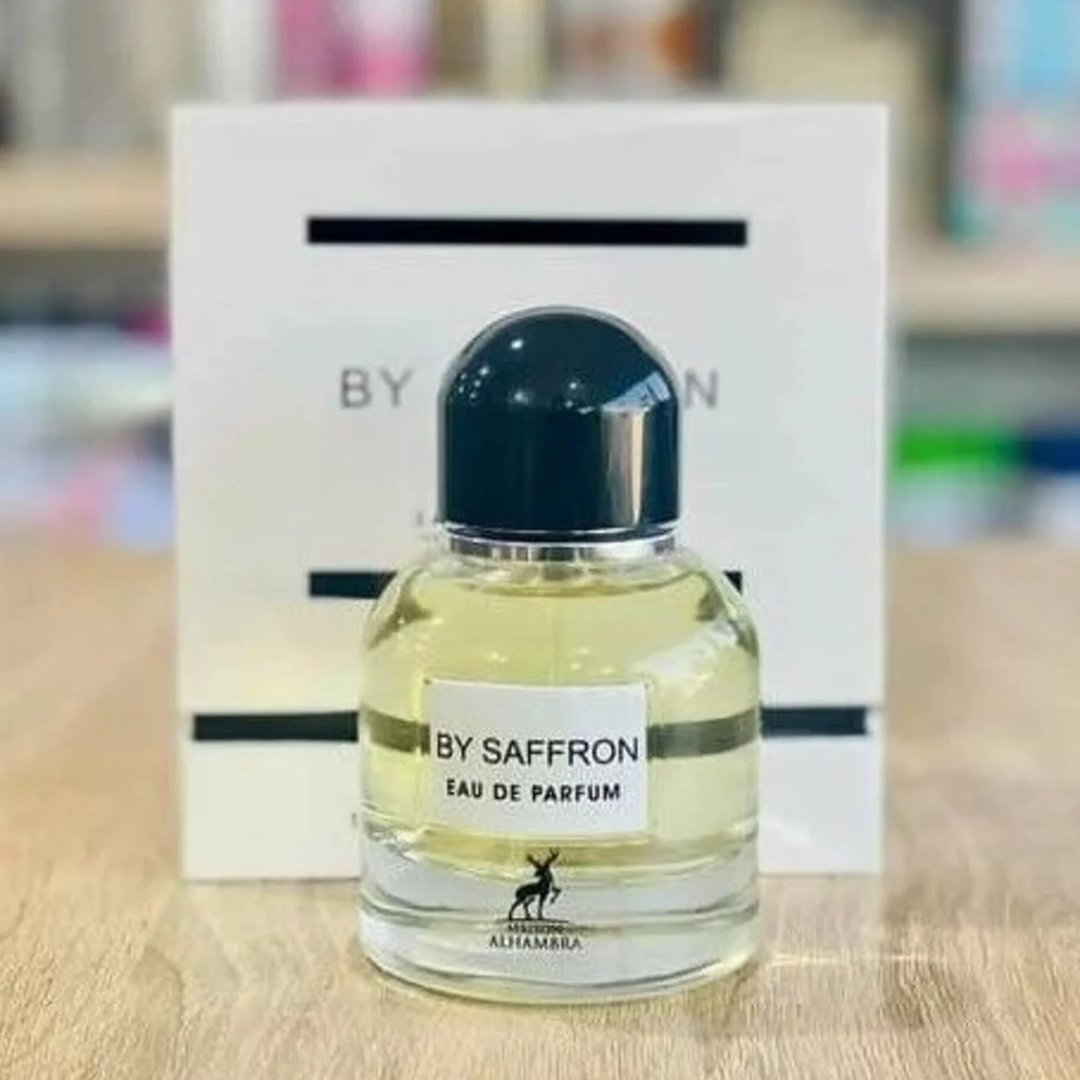 Maison Alhambra By Saffron by Maison Alhambra 100ml EDP Unisex — Botol minyak wangi kaca jernih berisi cecair kuning, penutup hijau gelap, dan label putih tertera 'BY SAFFRON EAU DE PARFUM' serta siluet rusa, dengan kotak putihnya di latar belakang.