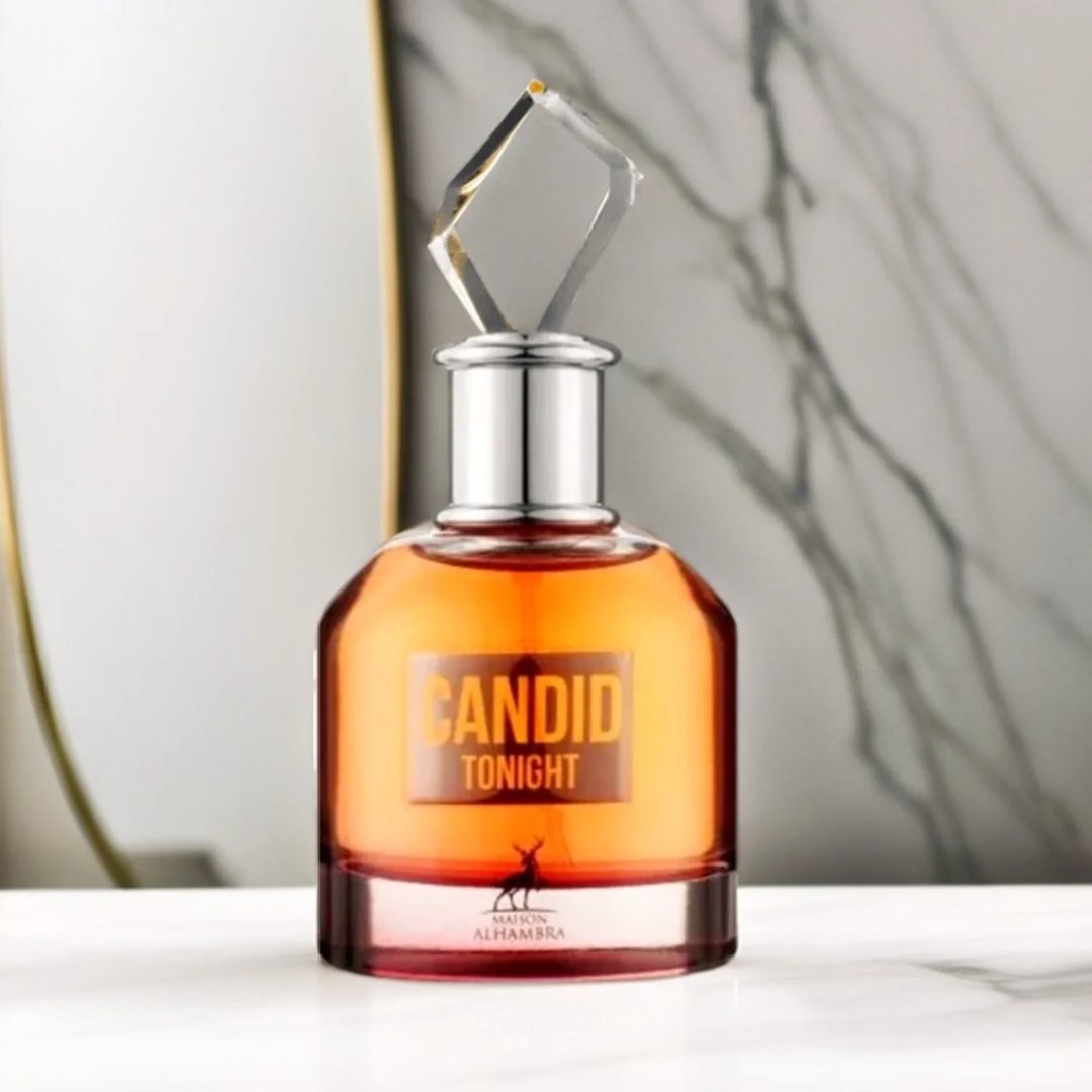 Maison Alhambra Candid Tonight by Maison Alhambra 100ml — A clear glass perfume bottle with orange liquid and a diamond-shaped clear cap, set against a marble-patterned background. | Maison Alhambra Candid Tonight by Maison Alhambra 100ml — Botol kaca jernih berisi cecair oren dan penutup berbentuk berlian jernih