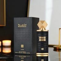 Lattafa Mashrabya — Kotak wangian hitam bertekstur dengan tulisan Arab emas dan corak geometri, bersebelahan botol hitam dan emas dengan penutup emas berfacets, di atas permukaan memantul dengan lilin kabur di latar belakang.