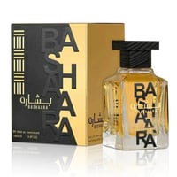 Ard Al Zaafaran Bashaara Eau De Parfum 100ml — A black and gold box with the brand name in large embossed letters stands next to a clear glass perfume bottle with a black cap. The perfume inside is golden. | Ard Al Zaafaran Bashaara Eau De Parfum 100ml — Kotak hitam dan emas dengan nama jenama dalam huruf timbul besar