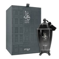 Zimaya Ghali Imperial Eau De Parfum 100ml by Zimaya — A dark grey textured box with a building facade pattern stands next to a dark, ornate perfume bottle with a tassel. | Zimaya Ghali Imperial Eau De Parfum 100ml by Zimaya — Kotak kelabu gelap bertekstur dengan corak fasad bangunan berdiri di sebelah botol minyak
