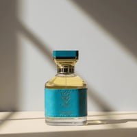 Bujairami Houdini by Bujairami 100ml Extrait — Clear glass perfume bottle with a turquoise leather-like band and gold accents, featuring a gold crown logo and text, set against a light background with soft shadows.