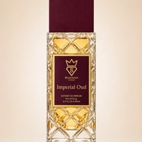 Bujairami Imperial Oud by Bujairami 100ml Extrait — Clear glass bottle with intricate geometric pattern, filled with golden liquid, topped with a deep red cap, and featuring a maroon label with gold text and a crown logo.