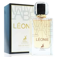 Maison Alhambra Leonie for Women by Maison Alhambra 100ml — A clear glass perfume bottle with a gold and black cap sits next to its white and black patterned box, both featuring gold lettering and a deer silhouette. | Maison Alhambra Leonie for Women by Maison Alhambra 100ml — Botol minyak wangi kaca jernih dengan