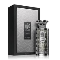 Zimaya Modhesh Noble 100ml — A silver patterned box stands next to a matching silver patterned perfume bottle, both with Arabic script and text. | Zimaya Modhesh Noble 100ml — Kotak corak perak berdiri di sebelah botol minyak wangi corak sepadan, kedua-duanya dengan skrip Arab dan teks.