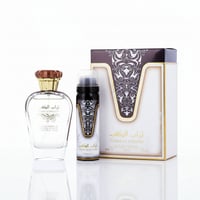 Ard Al Zaafaran Turab Al Dhahab — Clear perfume bottle, black spray can, and ornate box on a white reflective surface.