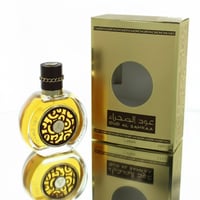 Lattafa Oud Al Sahraa by Lattafa Perfumes – 100 ml Unisex bottle with gold cap and chain detail, next to its gold box with a circular window, reflected on a white surface.