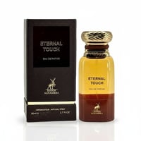 Maison Alhambra Eternal Touch Eau de Parfum — A brown textured box with gold lettering and a deer logo stands next to a clear glass perfume bottle with gold accents and a brown ombre effect.