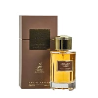 Maison Alhambra Exclusif Tabac – A brown box and a clear glass perfume bottle with golden cap and amber liquid, set against a white background.