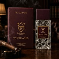 Bujairami Woodlands by Bujairami Extrait de Parfum 100ml — A dark red box and a clear glass perfume bottle with a dark red cap sit on a wooden surface. A lit cigar rests in an ashtray to the left, with smoke rising.