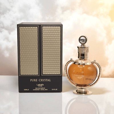 Lattafa Pride Pure Crystal EDP — A golden-accented perfume bottle with amber liquid, next to its black and gold patterned box, set against a soft, cloudy sky background.