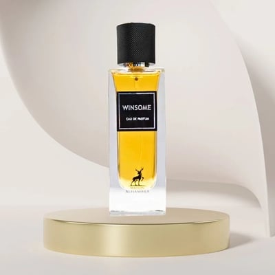 Maison Alhambra Winsome by Maison Alhambra 90ml EDP — A clear glass perfume bottle with golden liquid, black cap, and a deer silhouette logo, displayed on a gold podium against a curved cream background.