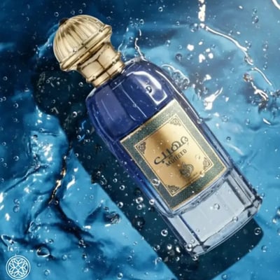 Al Wataniah Muheeb Perfume Man by Al Wataniah 100ml — A blue glass perfume bottle with a gold cap is submerged in water with splashes and bubbles. | Al Wataniah Muheeb Perfume Man by Al Wataniah 100ml — Botol kaca biru dengan penutup emas tenggelam dalam air dengan percikan dan buih.
