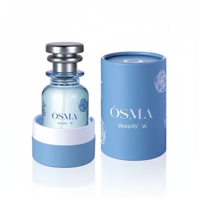 Osma Woody W Bergamot Leather 75ml EDP — A light blue glass perfume bottle with a silver cap, presented in a light blue cylindrical box with rose motifs. The bottle is in a white and light blue holder.