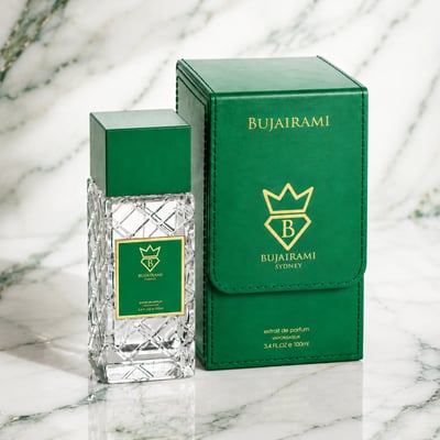 Bujairami Vibration by Bujairami 100ml Extrait de Parfum — Clear faceted glass perfume bottle with green cap and gold label, next to a matching green presentation box with gold logo and text, on a marble background.
