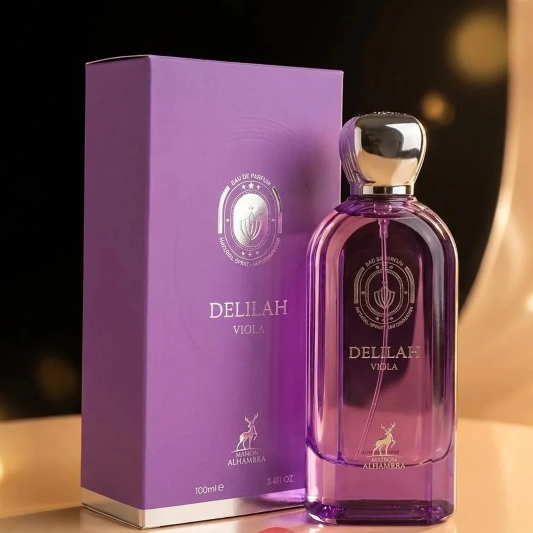 Maison Alhambra Delilah Viola 100ml — A purple perfume bottle and its matching box are displayed on a reflective surface with a blurred background. | Maison Alhambra Delilah Viola 100ml — Botol minyak wangi ungu dan kotaknya yang sepadan dipaparkan di atas permukaan reflektif dengan latar belakang kabur.