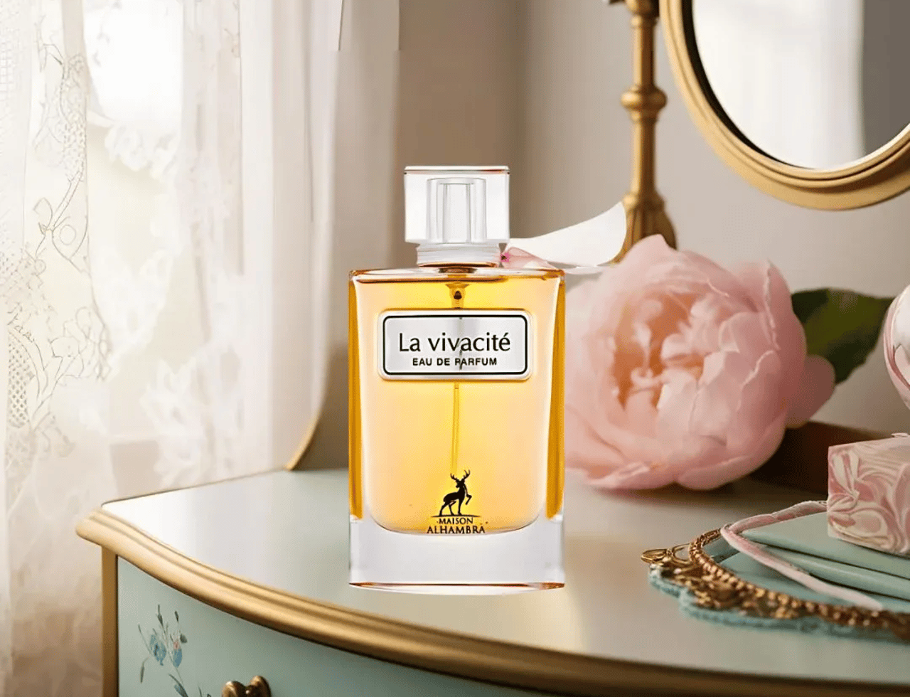 Maison Alhambra La Vivacite by Maison Alhambra 100ml EDP — Botol minyak wangi warna ambar bertudung putih dan reben merah jambu, diletakkan di atas meja solek antik dengan bunga ros merah jambu dan langsir renda.