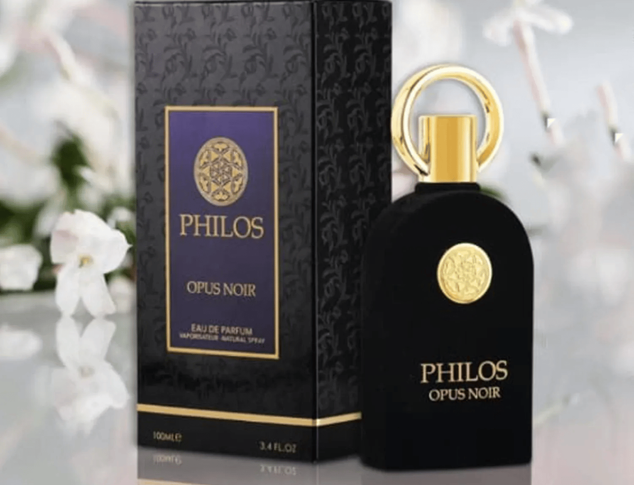 Maison Alhambra Philos Opus Noir — Botol minyak wangi hitam dengan perincian emas dan kotak bercorak sepadan, berlatar belakang bunga yang lembut.