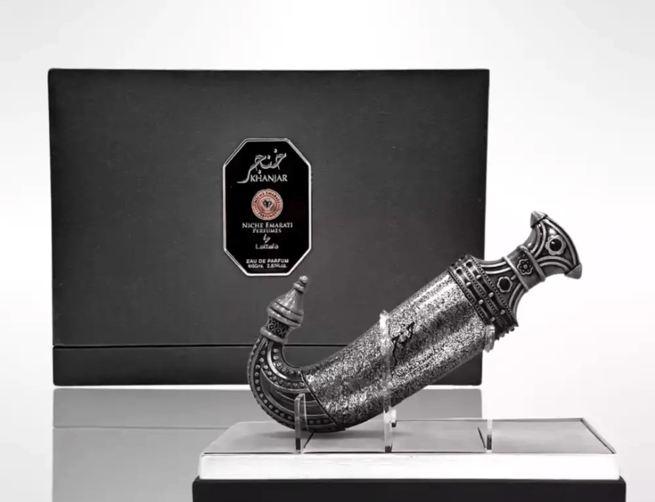 Niche Emarati Khanjar by Niche Emarati 85ml EDP — Ornate silver dagger-shaped perfume bottle displayed on a stand in front of a black presentation box with the brand logo.