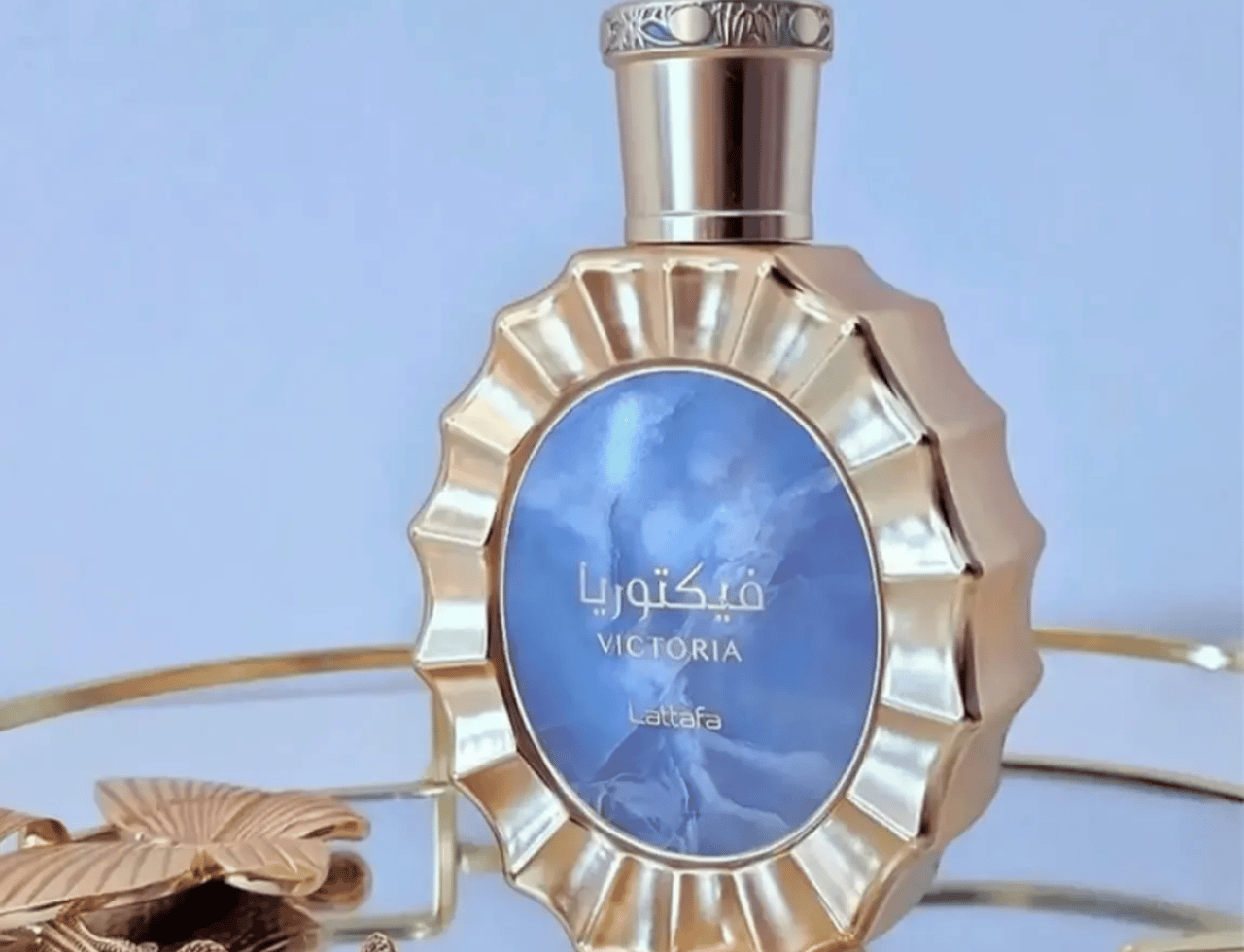 Lattafa Victoria by Lattafa 100ml EDP — Botol minyak wangi emas berlekuk dengan sisipan biru marmar, di atas dulang emas bersama rama-rama emas dan rantai leher