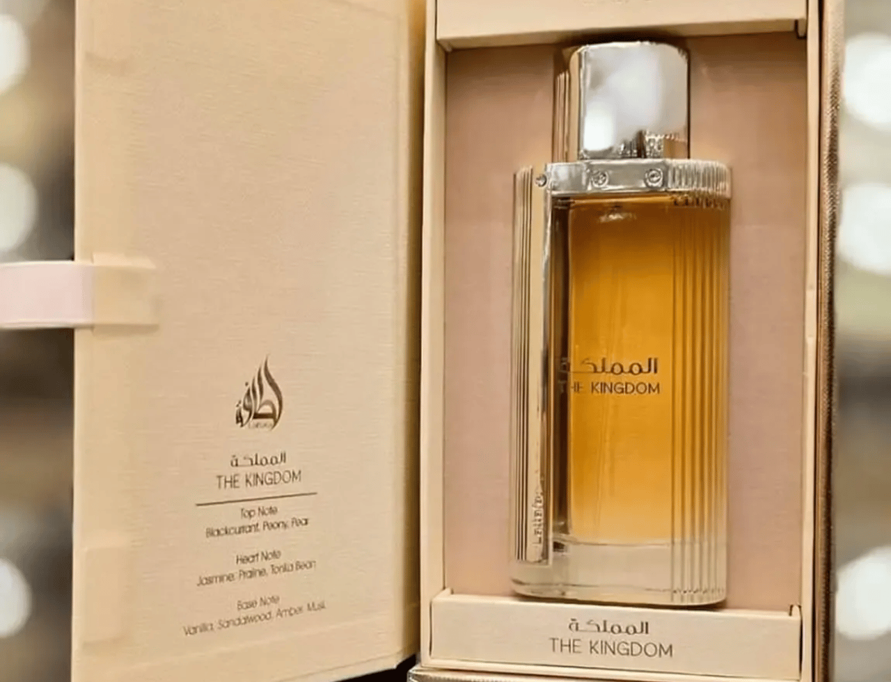 Lattafa The Kingdom Women by Lattafa 100ml EDP — Kotak emas dan krim mewah yang terbuka mendedahkan botol minyak wangi kaca beraksen emas berjalur dengan cecair keemasan di dalamnya, menunjukkan nota haruman pada kepak kiri.