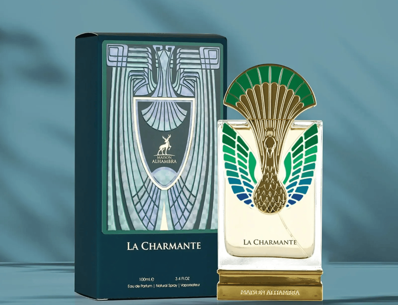 Maison Alhambra La Charmante by Maison Alhambra 100ml EDP — A perfume bottle with a peacock-inspired gold and green cap stands next to its matching dark teal box with art deco design.