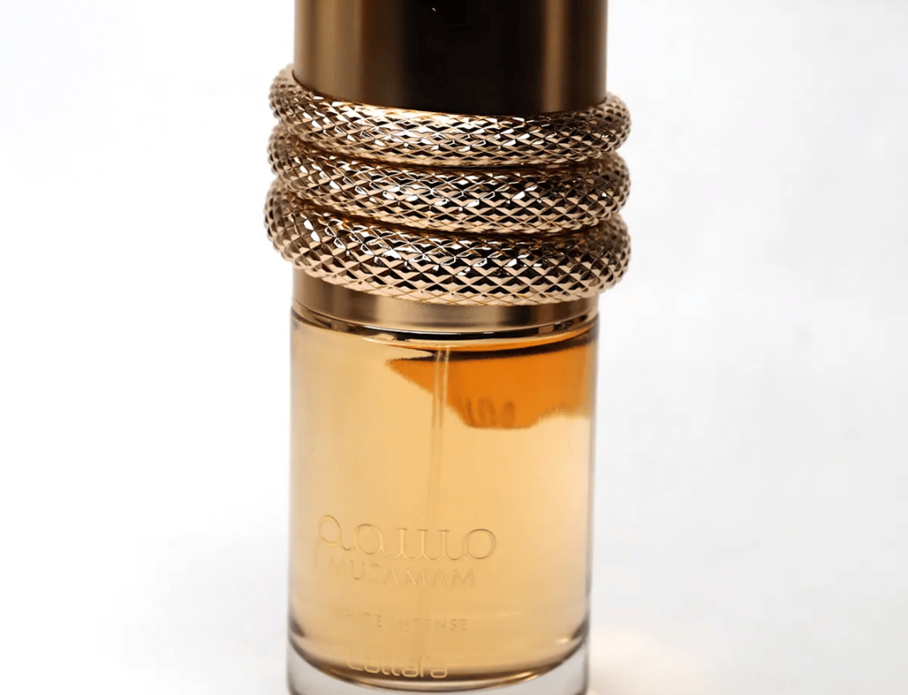 Lattafa Musamam Intense by Lattafa 100ml EDP — A tall, clear glass perfume bottle with golden liquid, featuring a gold cap wrapped in a textured, snake-like design. The brand name 'Musamam' and 'Lattafa' are visible on the bottle.