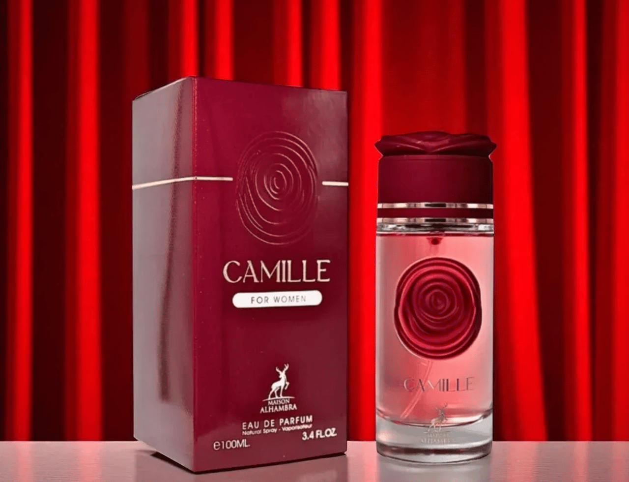 Maison Alhambra Camille by Maison Alhambra 100ml EDP — Kotak berwarna merah hati dan botol minyak wangi kaca jernih dengan rekaan bunga ros pada botol dan penutup, berlatar belakang langsir merah.