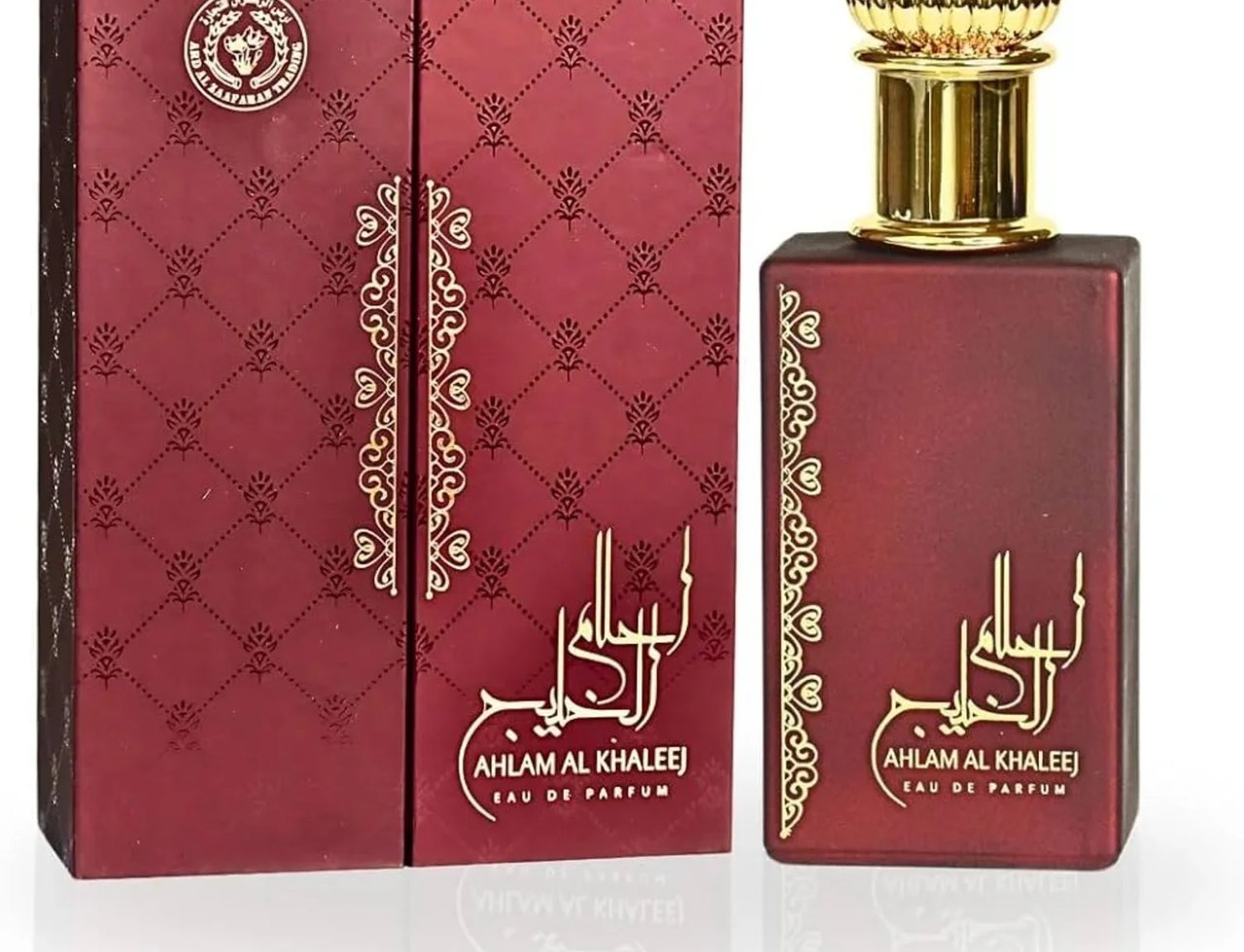 Ard Al Zaafaran Ahlam Al Khaleej 80ml by Ard Al Zaafaran — A maroon perfume bottle with a gold cap sits next to its matching maroon and gold patterned box, both featuring ornate gold Arabic calligraphy and text. | Ard Al Zaafaran Ahlam Al Khaleej 80ml by Ard Al Zaafaran — Botol minyak wangi berwarna merah marun dengan