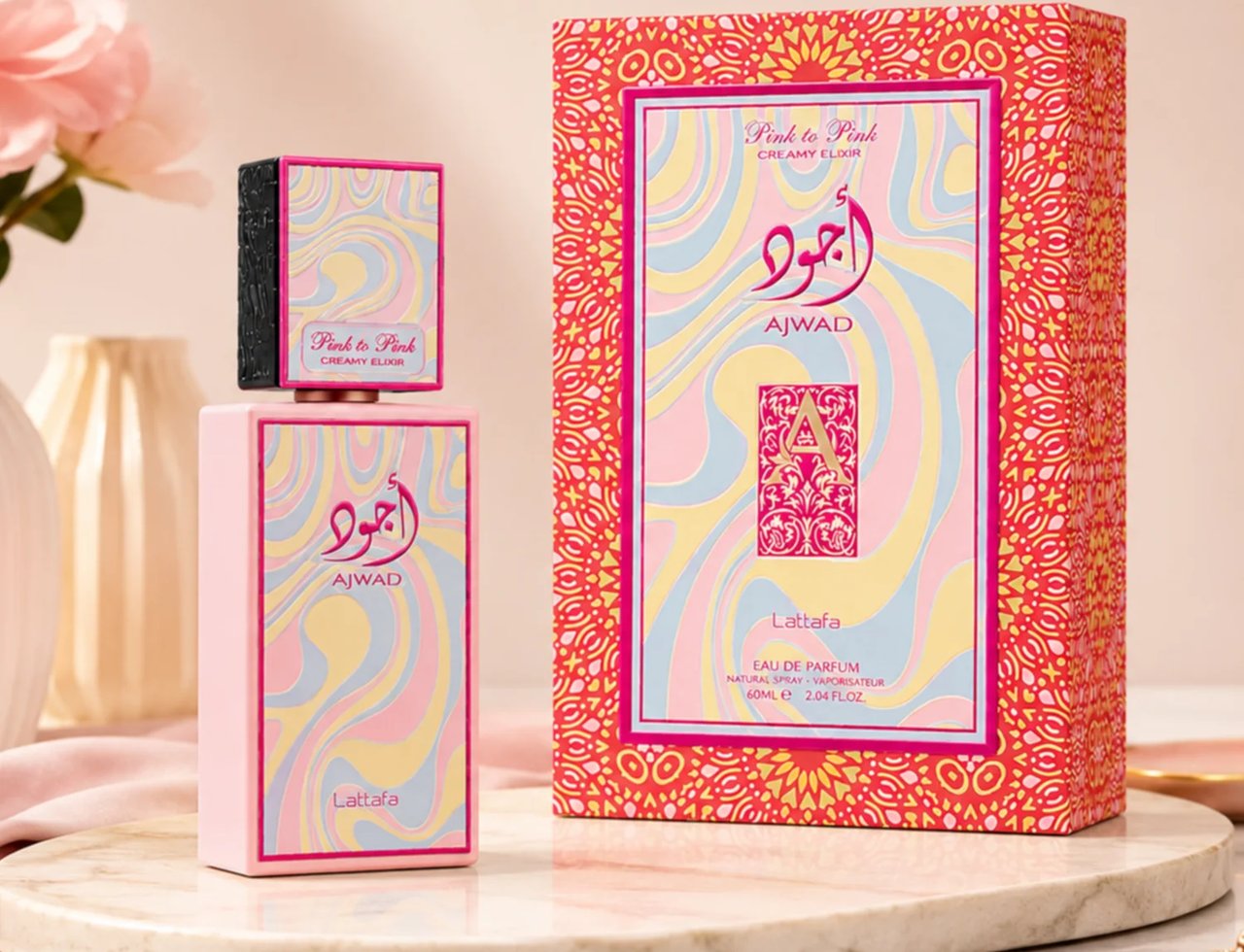 Lattafa Ajwad Pink 2 Pink Creamy Elixir — Pink perfume bottle and its box with wavy pastel design, placed on a marble surface with flowers in the background.