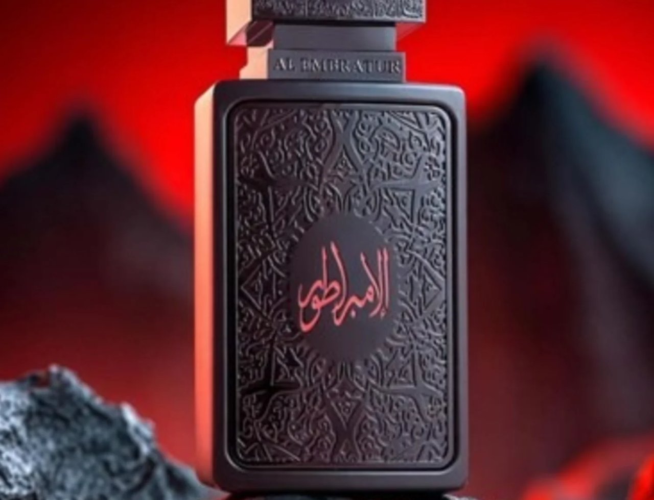 Zimaya Al Embratur Absolu Eau De Parfum 100ml — Black ornate bottle with Arabic script on a dark, rocky surface with a red, blurred background. | Zimaya Al Embratur Absolu Eau De Parfum 100ml — Botol hitam berukir dengan tulisan Arab di atas permukaan berbatu gelap dengan latar belakang merah kabur.