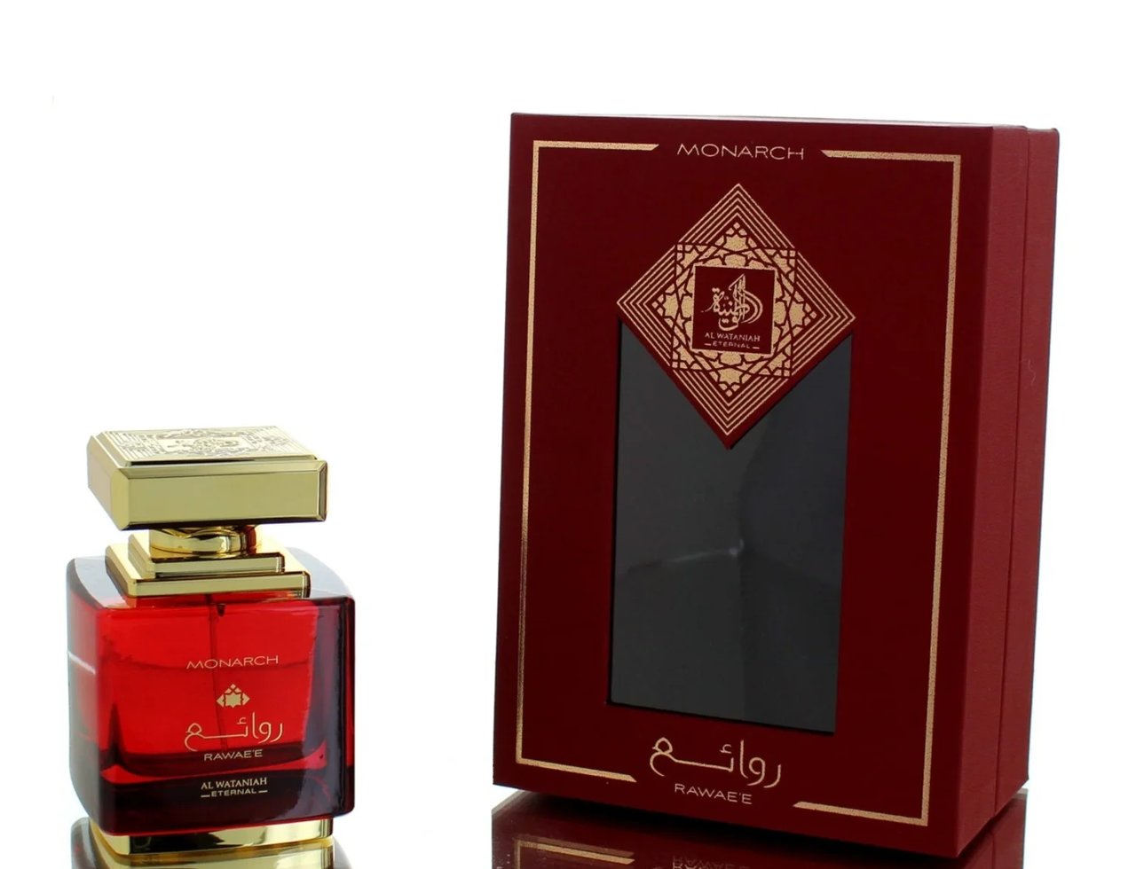 Al Wataniah Al Wataniah Rawaee Monarch Eau De Parfum 100ml — A red glass perfume bottle with a gold cap sits to the left of its matching red and gold presentation box with a window. | Al Wataniah Al Wataniah Rawaee Monarch Eau De Parfum 100ml — Botol kaca merah dengan penutup emas duduk di sebelah kiri kotak