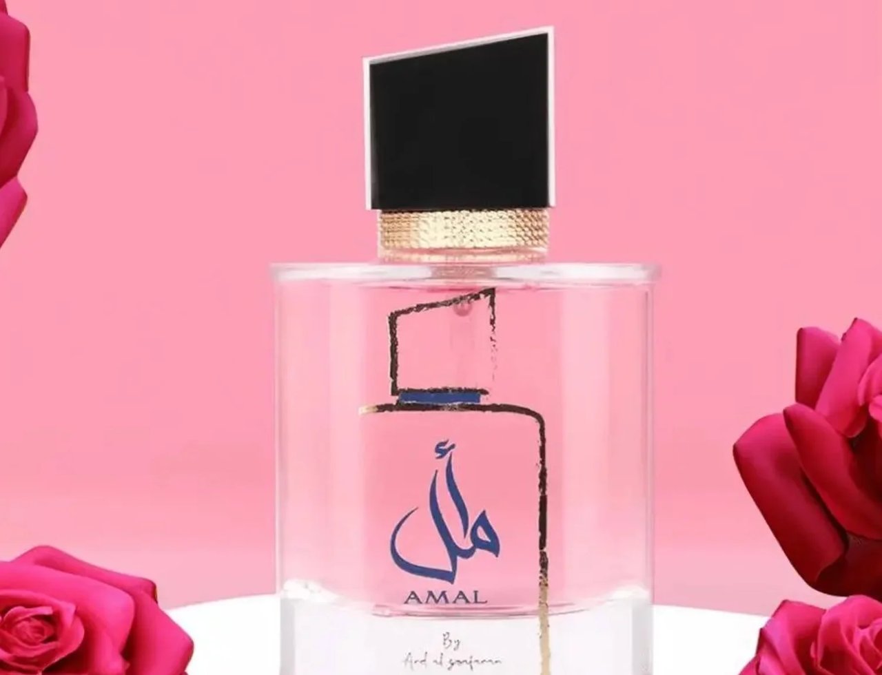 Ard Al Zaafaran Amal Ard Al Zaafaran 100ml Women — Clear glass perfume bottle with pink liquid, black cap, gold accents, and Arabic calligraphy on a pink background with pink roses.