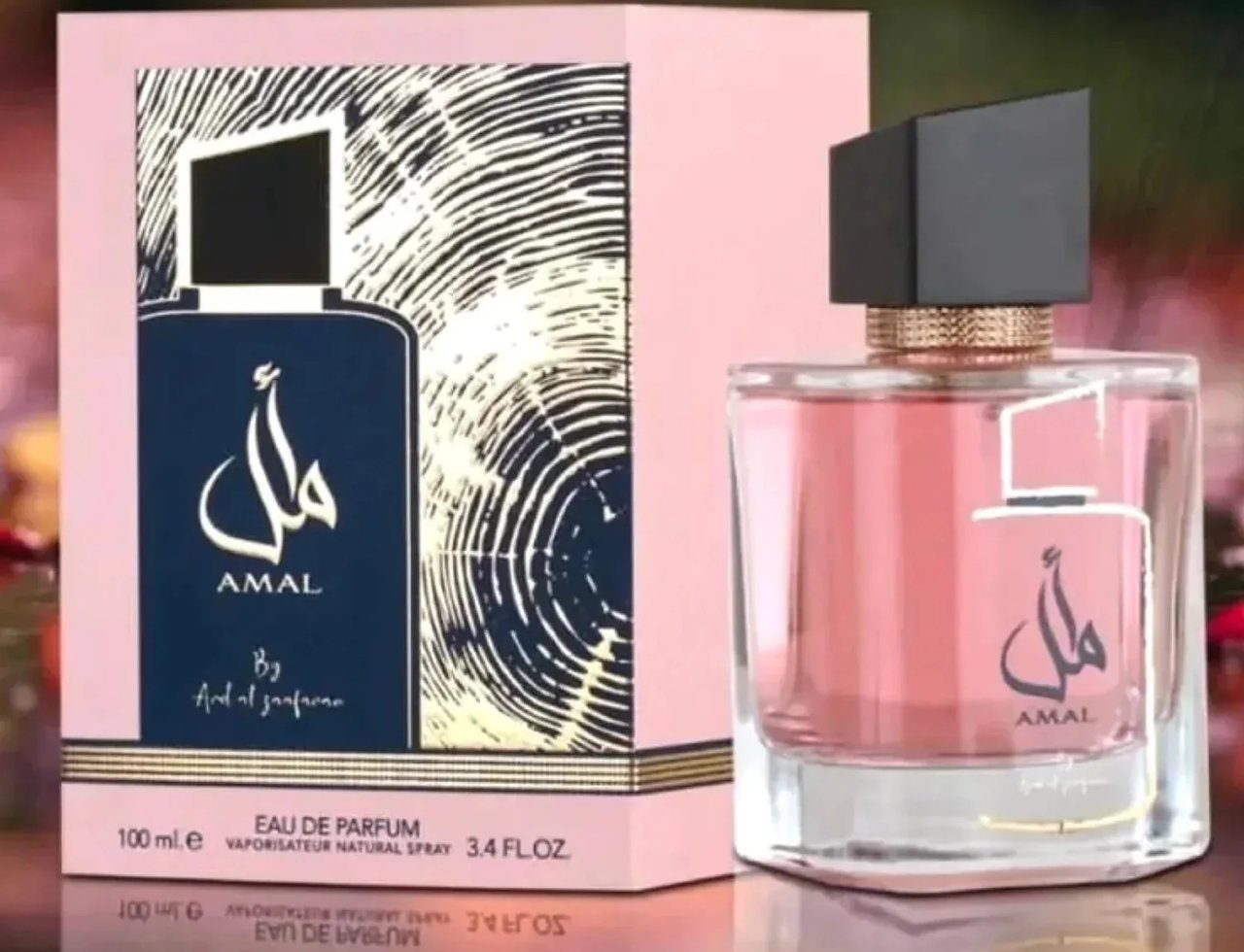 Ard Al Zaafaran Amal Ard Al Zaafaran 100ml Wanita — Kotak merah jambu corak bijian kayu dan botol biru gelap dengan kaligrafi Arab, bersebelahan botol minyak wangi kaca merah jambu bertutup hitam.
