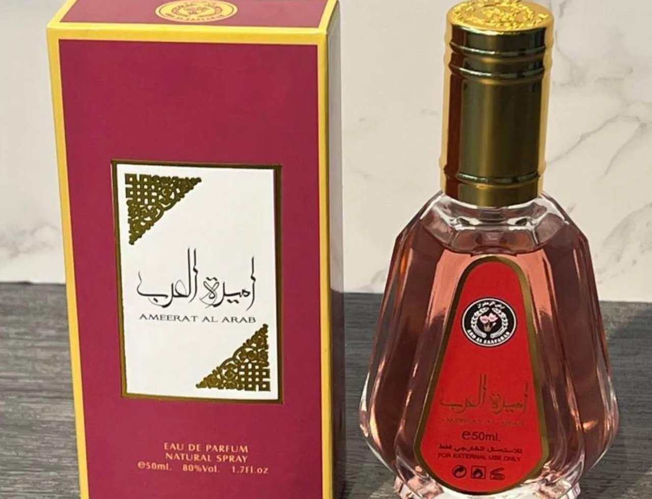 Ard Al Zaafaran Ameerat Al Arab Princess of Arabia 50ml — A maroon and gold box sits next to a faceted glass perfume bottle with a gold cap and a red label. | Ard Al Zaafaran Ameerat Al Arab Princess of Arabia 50ml — Kotak merah marun dan emas terletak di sebelah botol minyak wangi kaca berfaset dengan penutup emas