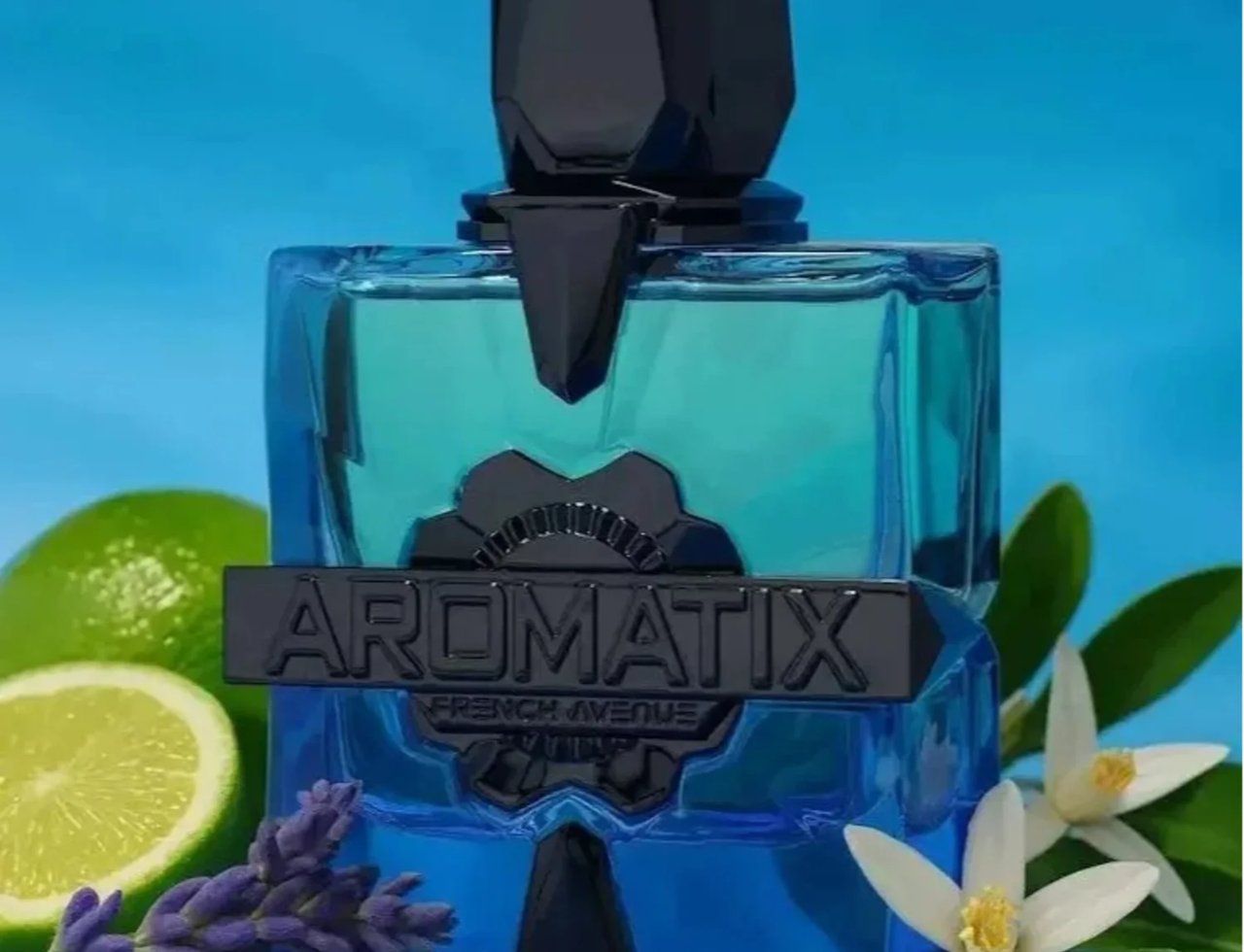 French Avenue Aromatix Magnetiq by French Avenue 100ml — Botol minyak wangi kaca biru dengan penutup dan perincian geometri hitam, dikelilingi hirisan limau, tangkai lavender, dan bunga putih berlatar belakang biru terang.
