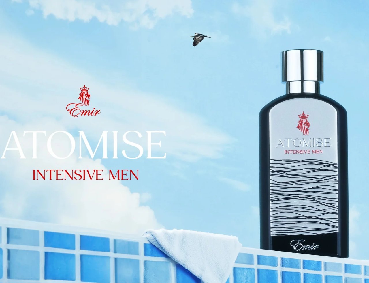Paris Corner Atomise Intensive Men by Emir Paris Corner 100ml — A bottle of Atomise Intensive Men perfume stands on a blue tiled surface, with a white towel draped over it. A bird flies in the sky with clouds in the background. | Paris Corner Atomise Intensive Men by Emir Paris Corner 100ml — Sebotol minyak wangi