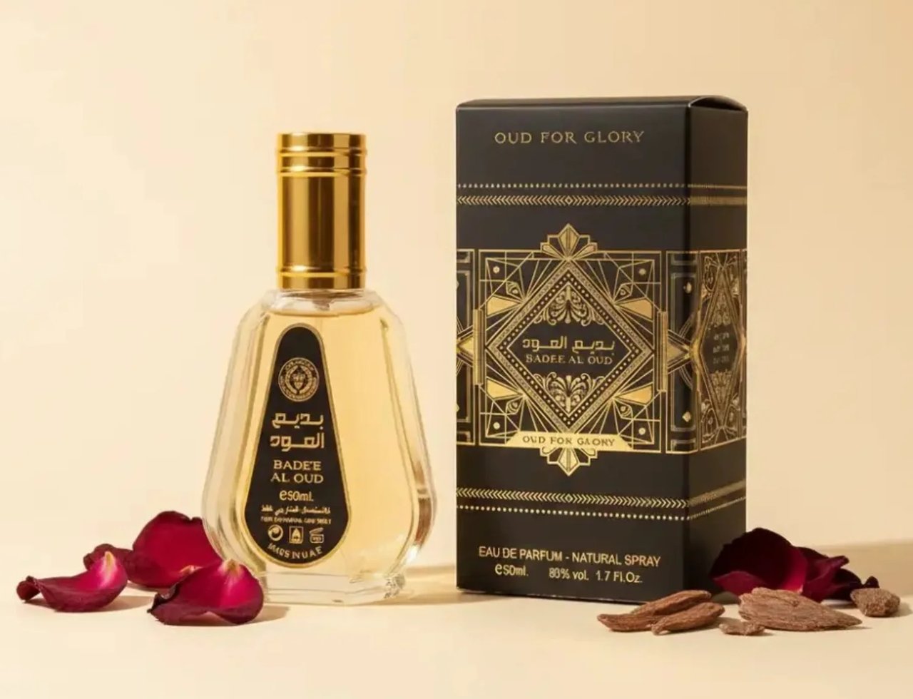 Ard Al Zaafaran Badee Al Oud Eau De Parfum 50ml — Botol kaca jernih berisi cecair keemasan, bertudung emas, diletakkan di sebelah kotak hitam berhias emas. Kelopak mawar merah dan ketulan kayu gaharu turut kelihatan.