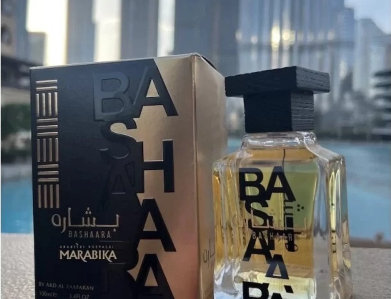 Ard Al Zaafaran Bashaara Eau De Parfum 100ml by Ard Al Zaafaran — Kotak wangian hitam keemasan dan botol kaca jernih dengan penutup hitam, latar belakang bangunan moden