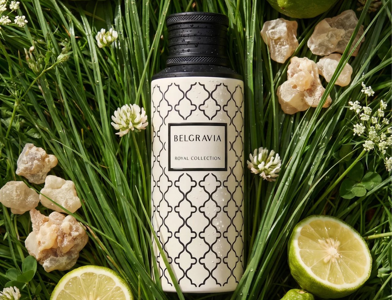 Maison Asrar Belgravia by Maison Asrar Eau de Parfum — Botol bertutup hitam dan badan putih bermotif, dikelilingi rumput, hirisan limau, limau utuh, dan ketulan resin berwarna ambar.