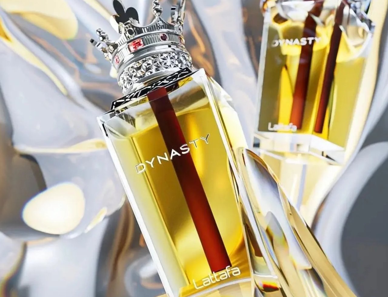 Lattafa Dynasty by Lattafa 100ml EDP Unisex — Botol minyak wangi kaca jernih berisi cecair kuning dan batang merah di dalam, kemasan penutup mahkota perak bertatah permata merah. Botol condong, dengan botol kedua kabur di latar belakang, berlatar fabrik perak dan emas berkilauan.