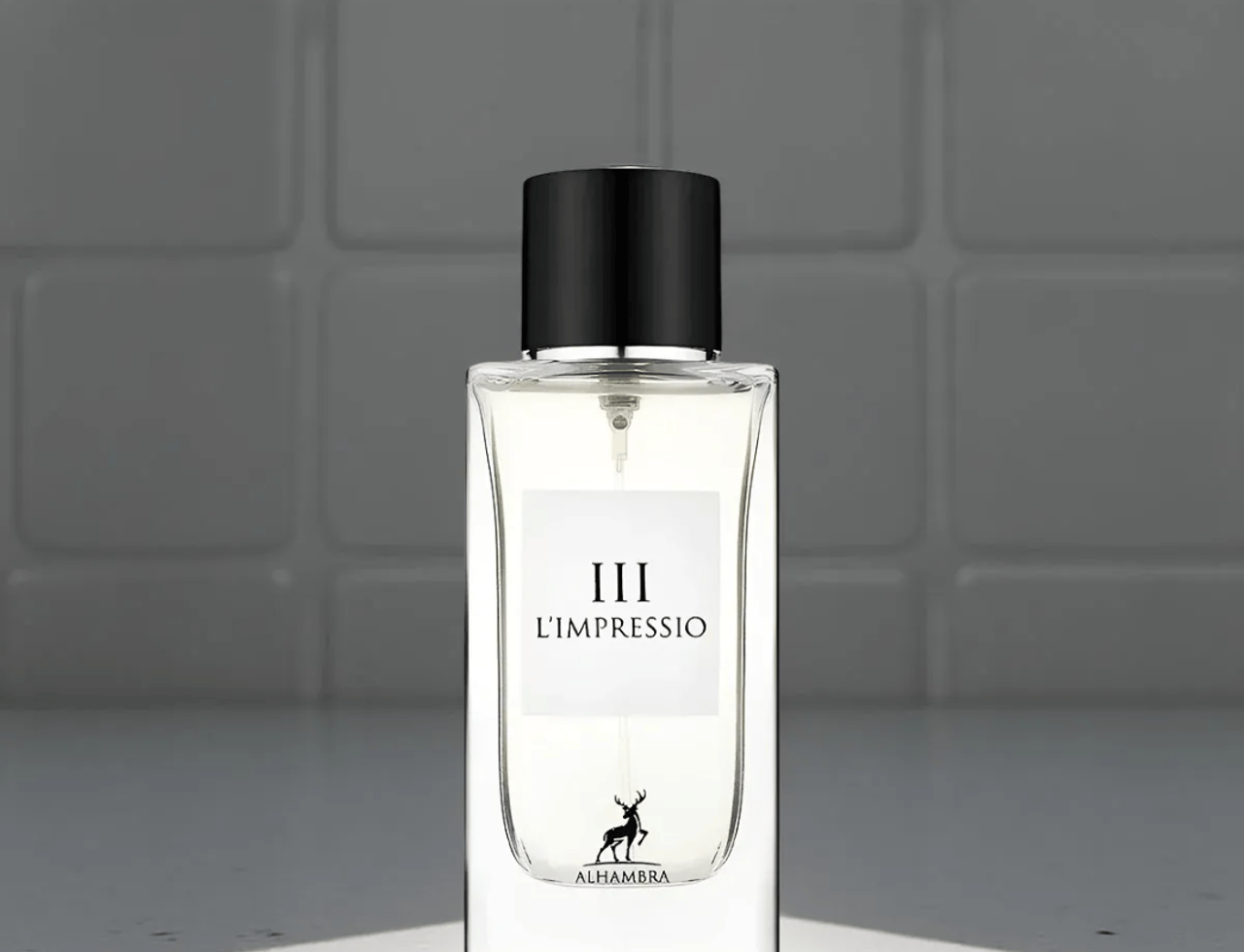 Maison Alhambra L'Impressio Pour Femme — Botol minyak wangi kaca jernih dengan label putih bertulis hitam dan siluet rusa, bertudung penutup hitam, berlatar belakang dinding jubin.