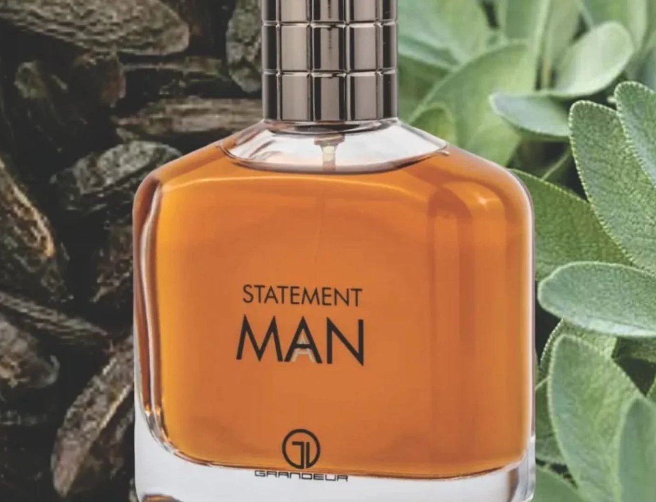 Grandeur Statement Man Eau De Parfum 100ml — A clear glass perfume bottle with amber liquid, a silver textured cap, and black text reading "STATEMENT MAN" and "GRANDEUR" | Grandeur Statement Man Eau De Parfum 100ml — Botol kaca jernih berisi cecair berwarna ambar, penutup bertekstur perak, dan teks hitam bertulis