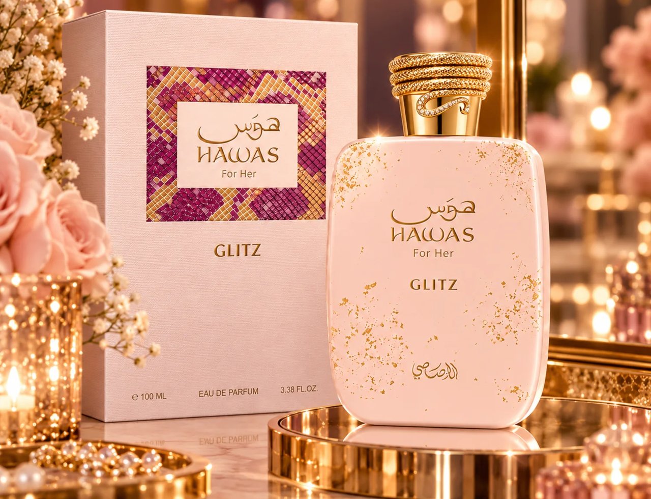 RASASI Hawas Glitz by Rasasi 100ml EDP — Pink bottle with gold glitter accents and ornate gold cap, next to its matching pink box with a patterned insert, surrounded by soft pink roses and lit candles.